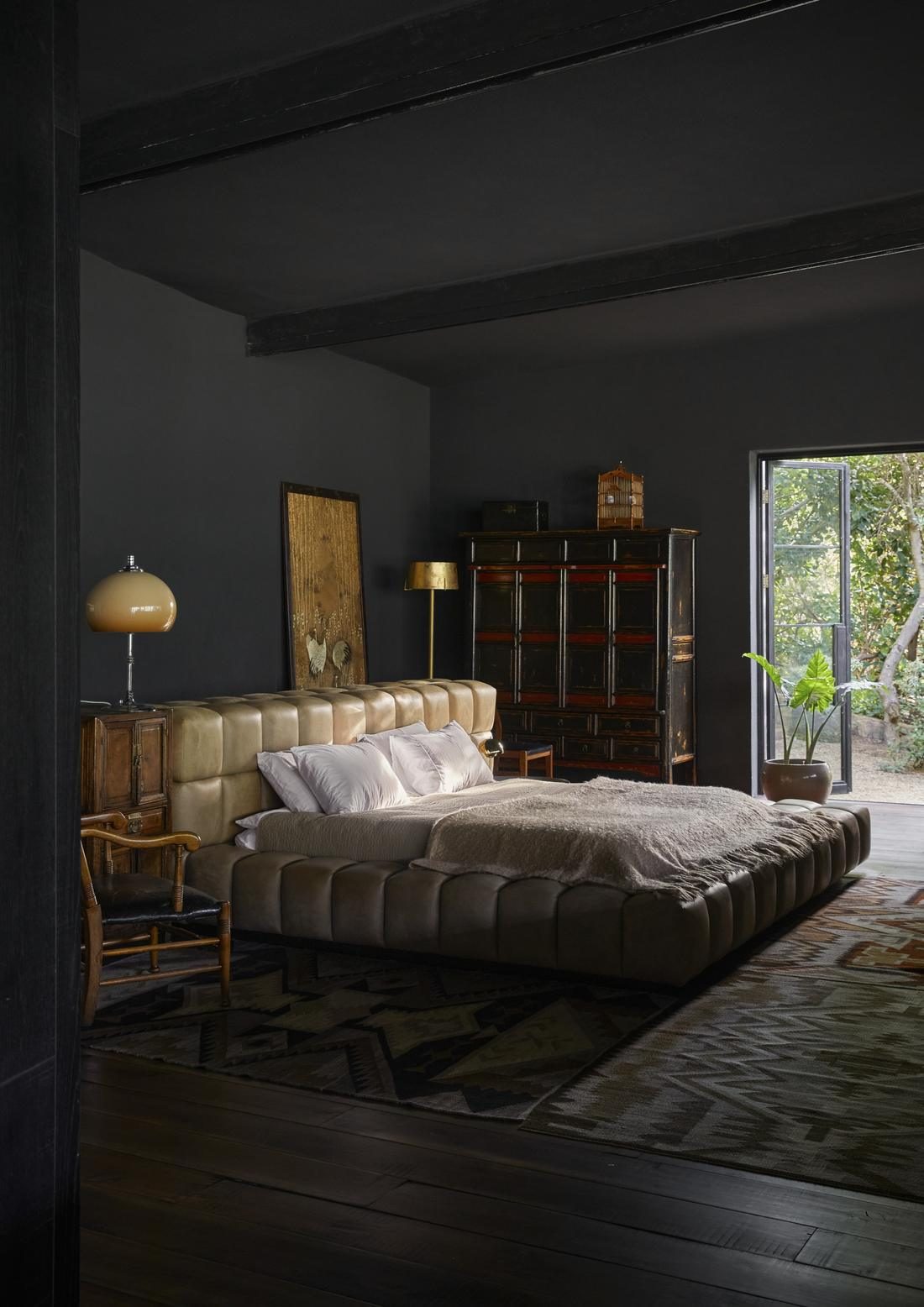 Dark walled bedroom with a low leather bed, brass lamps and a doorway to the garden