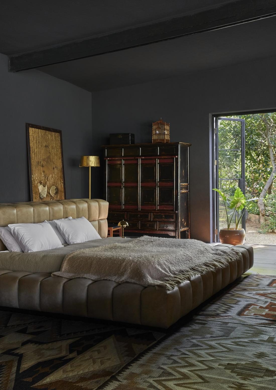 Bedroom with a low leather bed, an antique cabinet and an open door to the garden
