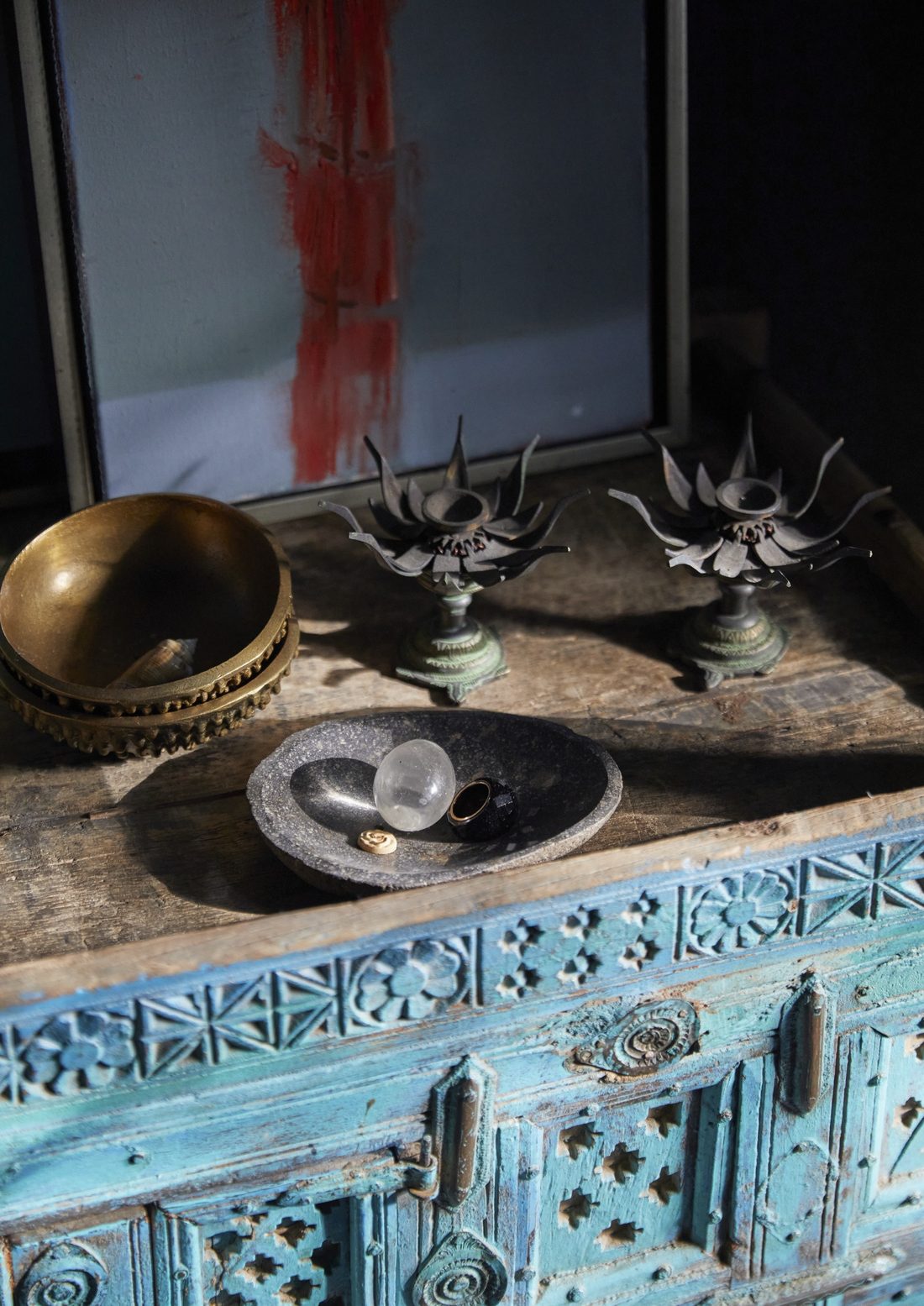 Carved blue painted chest topped with brass bowls, lotus candle holders and a stone dish holding a crystal ball
