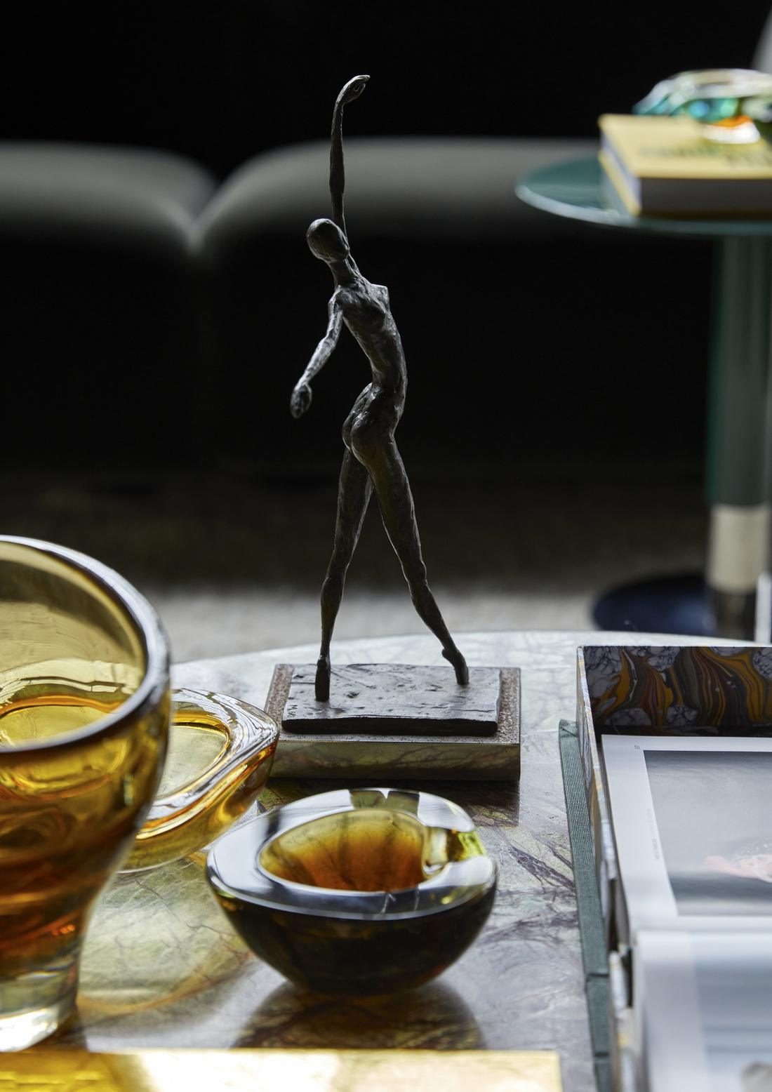 Bronze figure of a dancer on a marble table beside amber glass bowls