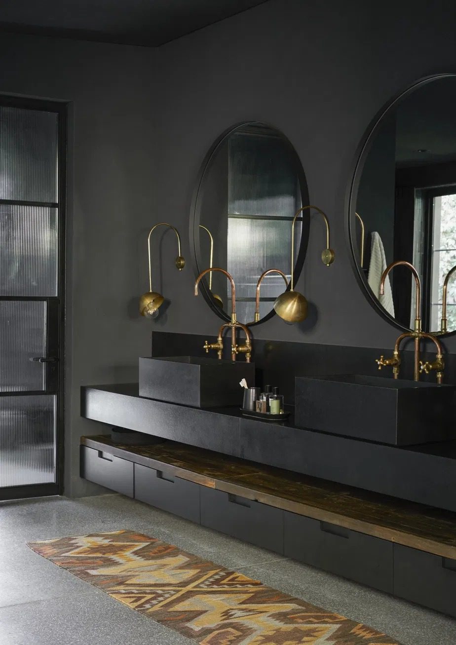Bathroom with two black stone basins, copper taps, round mirrors and brass wall lights